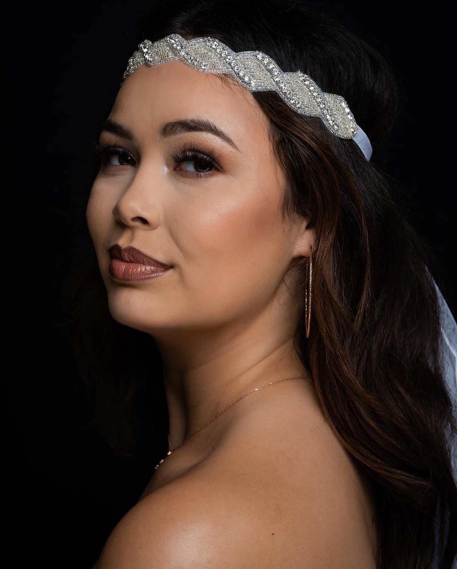 A bride in a veil and crystal headband, turned over her shoulder, wearing warm bronze eye makeup and a soft rose lip